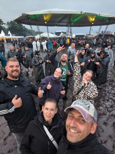 Gruppe von Menschen bei einem Festival, freundlich, im Matsch, unter einem überdachten Bereich.