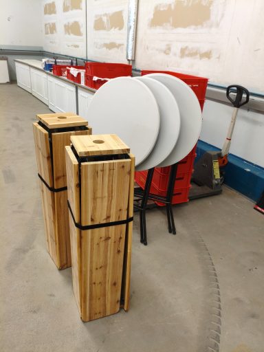Zwei stapelbare Holztische stehen neben drei runden, weißen Tischen.