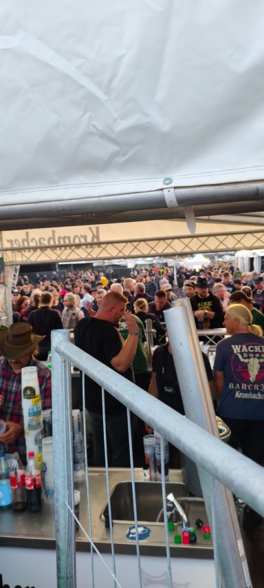Blick auf eine Menschenmenge hinter einem Stehtisch auf einem Festival.
