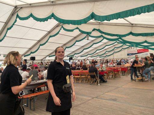 Festzelt mit Gästen, zwei Kellnerinnen in schwarzer Kleidung stehen im Vordergrund.