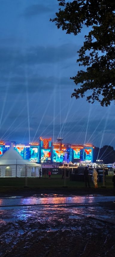 Bunte Lichtinstallationen leuchten über einem Festivalgelände bei Dämmerlicht.