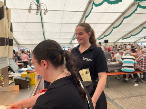 Zwei Frauen in schwarzen T-Shirts arbeiten in einem Zelt bei einem Fest.