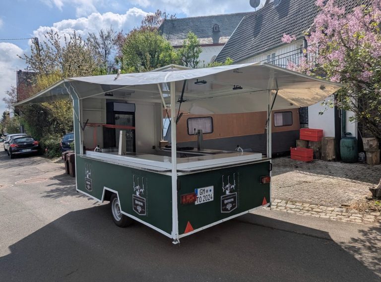 Grüner Verkaufsanhänger mit Markise und Beleuchtung in der Dämmerung.