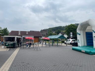 Marktplatz mit Hüpfburg, Tischen und Stühlen, umgeben von Bäumen und Gebäuden.