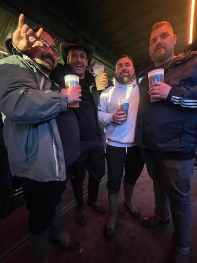 Vier Männer posieren in einer Bar, jeder hält ein Getränk in der Hand.