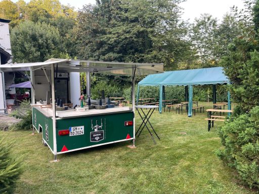 Grüner Verkaufsstand im Freien mit überdachtem Sitzbereich und Bänken.