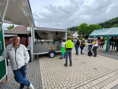Menschen stehen in einer Schlange vor einem Imbisswagen, bewölkter Himmel.