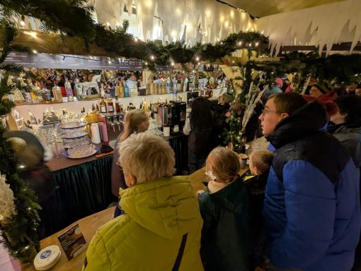 Menschen betrachten festlich dekorierte Stände auf einem Weihnachtsmarkt.