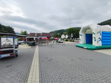 Ein Platz mit einem Hüpfburg, Pavillons und Tischen in einer ländlichen Umgebung.