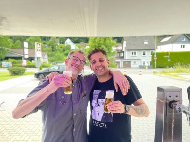 Zwei Männer stehen lächelnd und mit Biergläsern in den Händen zusammen.