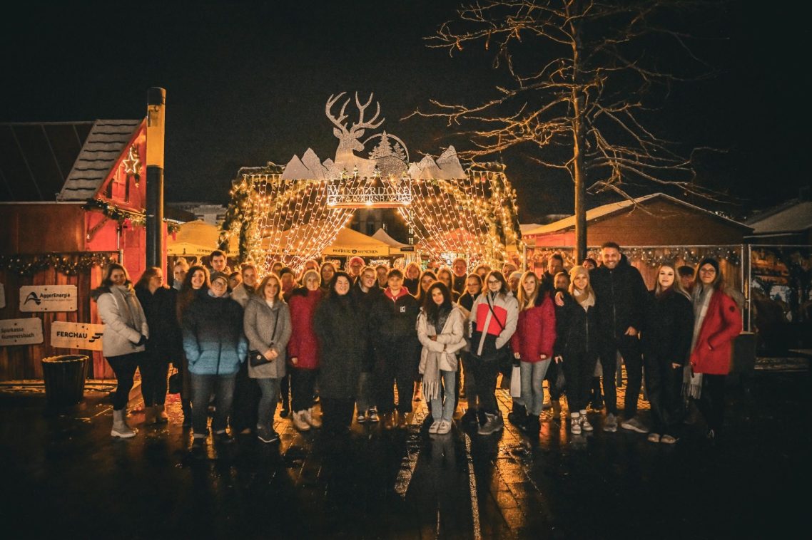 Team vor einem festlich dekorierten Weihnachtsstand bei Nacht.