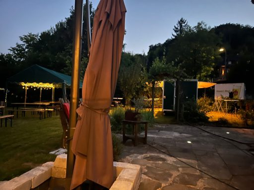 Ein Garten mit Beleuchtung, Tischen und einem Sonnenschirm bei Dämmerung.