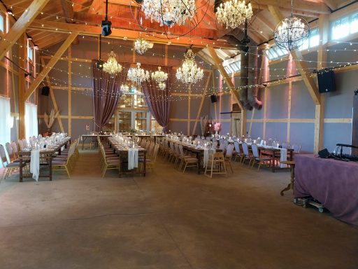 Festlich dekorierter Saal mit langen Tischen, Kronleuchtern und Holzstützen.