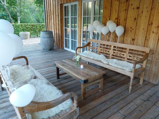 Holzboden mit zwei Bänken, einem Tisch und weißen Ballons im Hintergrund.