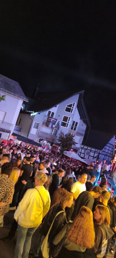 Bunte Feststimmung mit vielen Menschen und festlich dekorierten Ständen bei Nacht.
