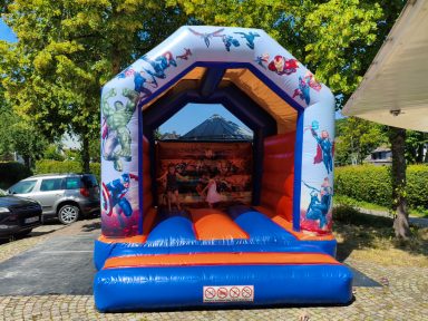Bunte Hüpfburg mit Comicfiguren, orange und blaue Sprungfläche im Freien.