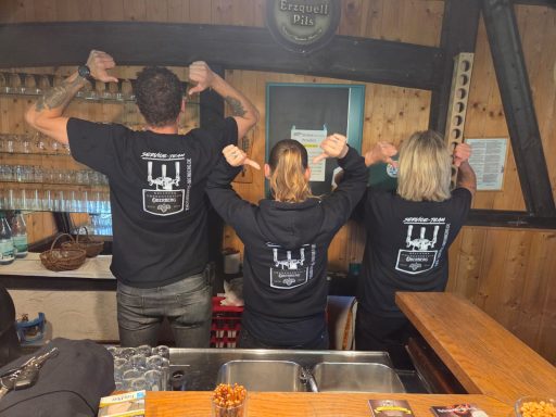 Drei Personen in schwarzen T-Shirts zeigen mit den Händen nach oben, Rücken zur Kamera.