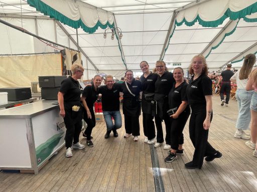 Gruppe von acht Personen in schwarzer Kleidung, lächelnd in einem Zelt.
